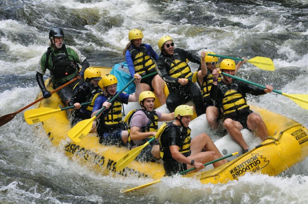 A group of U N E students having fun while white water rafting down a river in Maine